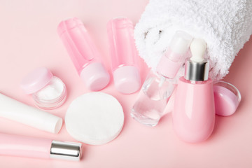 Face care products (tonic or lotion, serum, cream, micellar water, cotton pads) covered in towel on pink, powder background. Freshness and face care. Skin cleansing and anti-age care. Female cosmetics