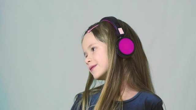Pretty smiling cild girl listening to music in big pink earphones.