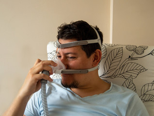 Young man is worried about using nasal CPAP mask. Man with sleep apnea disease doesn't want to use cpap machine.