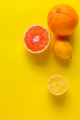 Top view whole and sliced ripe orange, grapefruit and lemon on a yellow surface, concept of health...
