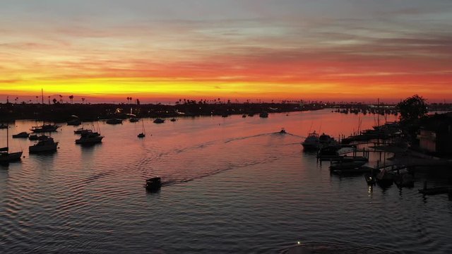 Aerial shot or drone view of Newport Beach Orange County California harbor Pacific ocean and sea with boats below during stunning sunset with pink and orange sky.