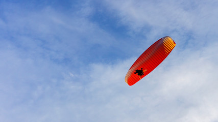 Alone paraglider flying in the classic blue sky against the background of clouds. Paragliding in the sky on a sunny day