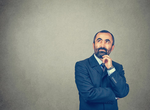 man with dark suit tie blue shirt watch touching chin, looking up.