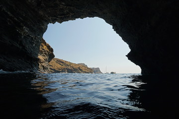 Rocky coast with some boats seen from water surface inside a large cave, Mediterranean sea, Spain, Costa Brava, Catalonia, Cap de Creus