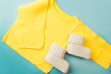 Yellow shirt for baby boy and knitted booties on blue background. New-born child clothes concept. Top view.