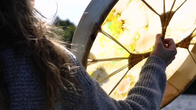 A short movie showing close up details of a person playing a scared drum, native powwow handcrafted artifact with stretched rawhide membrane, backlit