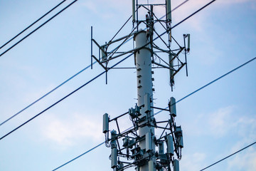 A close up detailed view of multiple antenna housed on a monopole. Overhead cables cross a cellular...