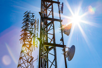 Bright sun shine over two cell site towers, radio and GPS transmitter and receiver, associated with...