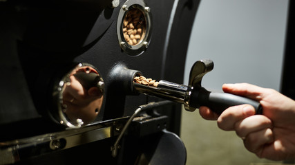 Fototapeta na wymiar Coffee Roasting Technology. A man controls the coffee roasting machine. Close-up.