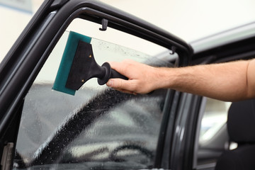 Worker washing tinted car window in workshop, closeup