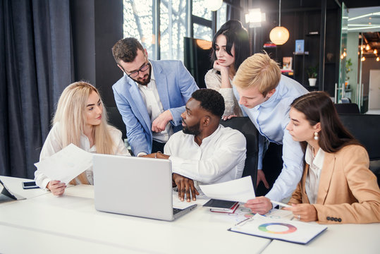 Mixed races corporate young coworkers which discussing business strategy of their successful company using laptop at the boardroom table.