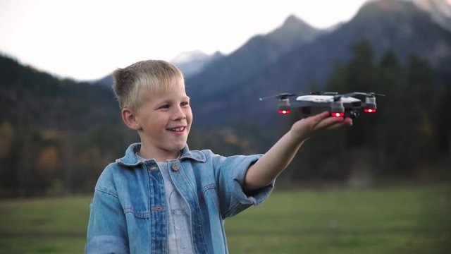 Portrait of happy boy very happy and smiling gift the background of a bright sky and mountains holds a white quadro copter drone plane in his hand and start him playing .