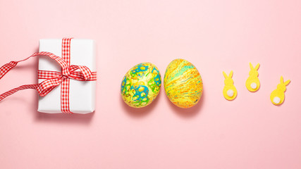 Easter eggs, white gift box with red gift bow and yellow rabbits on pink background. Flat lay top view Easter concept