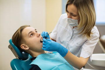 Dentist doing teeth checkup of man in a dental chair at medical stomatology clinic.