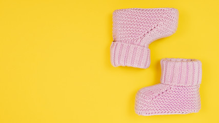 Pink cute booties for newborn baby. Baby girl shoes on yellow background. Banner 16x9, copy space.