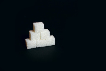 Six sugar cubes on a black background, a sweet additive to taste or a harmful and dangerous ingredient, diabetes, place for text