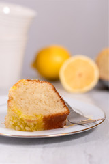 Lemon Cake Slice on White Plate with Lemons in Background