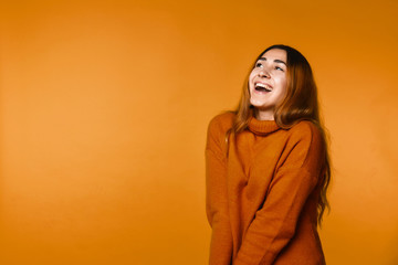 Sincerely smiling redhead caucasian girl dressed in wool pullover of ocher color on the orange...