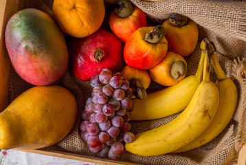 fruits in wooden basket: cashew, orange, grape, banana, mango and papaya