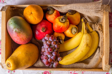 fruits in wooden basket: cashew, orange, grape, banana, mango and papaya