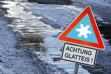 Eine eisglatte Straße im Winter mit einem Schild Achtung Glatteis!