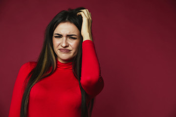 Beautiful brunette baffled caucasian girl dressed in red pullover is scraping her hair withhand  on...