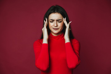 Beautiful brunette caucasian girl dressed in red pullover with painful headache on the pink...