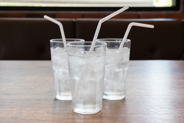three glasses of cold water with ice cube and white plastic straw on woonden table in asian restaurant.