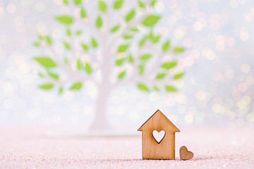 Wooden icon of house with hole in form of heart with green tree on white background with bokeh lights. - 314174094