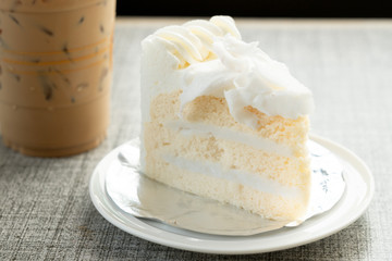 vanilla cake on plate and ice coffee on wooden table in cafe shop