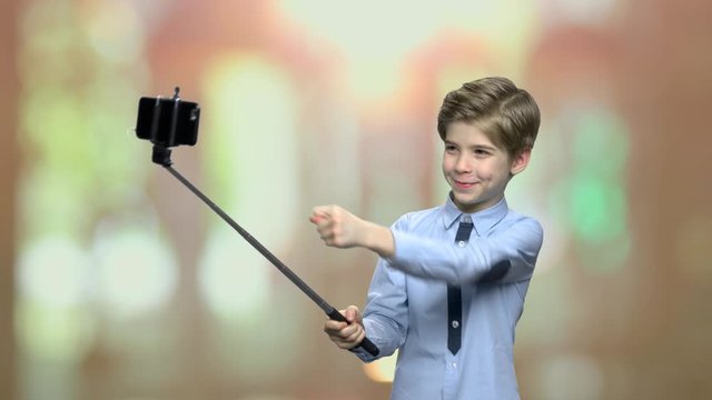 Little boy taking selfie with monopod. Child showing fig sign while posing for camera. Modern lifestyle and technology concept.