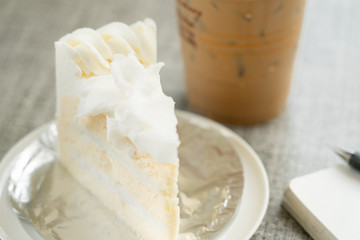 vanilla cake on plate and ice coffee on wooden table in cafe shop