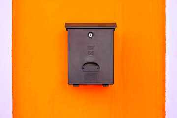 Simple black mail box on a vibrant warm red orange background.