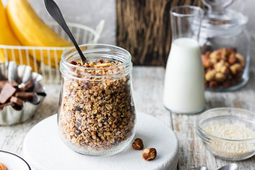 Chocolate banana granola with nuts in a glass jar on a light background