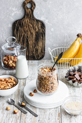 Chocolate banana granola with nuts in a glass jar on a light background