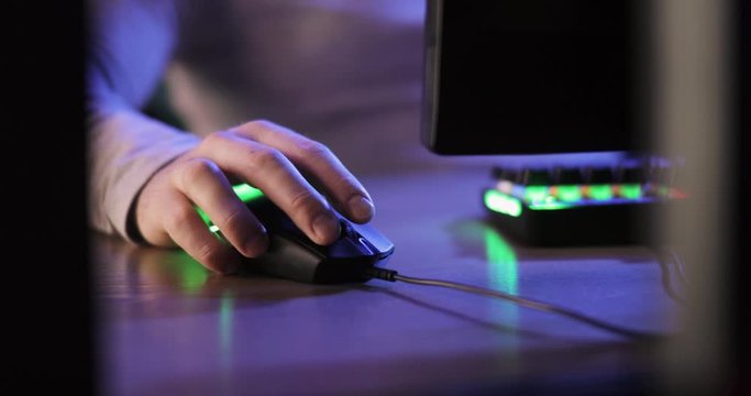 Concept of dependence on computer games and relaxing. Man gamer playing computer games pressing mouse sitting at table, hands closeup. Way of escaping from reality, online life instead real life.