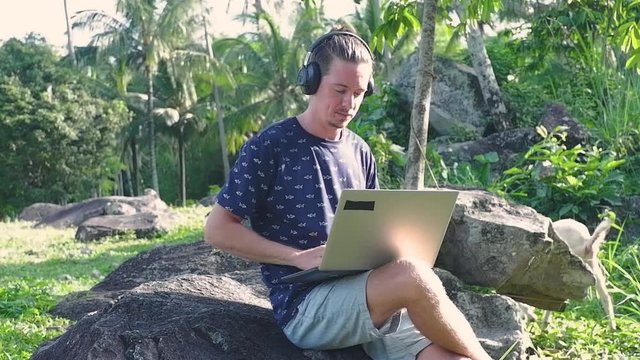 A man is sitting on the stone while working as a freelancer. He is doing his work in the mountain.