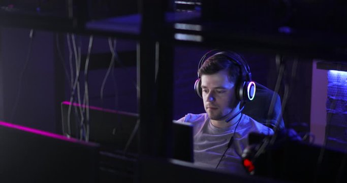 Portrait of man gamer talking online with somebody with headset playing game looking at screen in dark. Concept of relax and dependence on computer games. Online gaming in network.