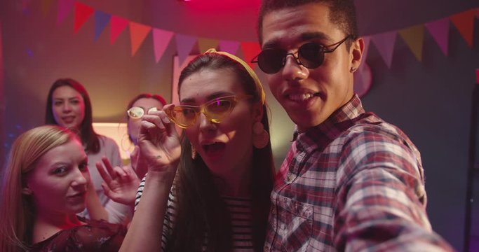 Close up of the young cheerful couple smling and taking selfie photo with their happy friends and big golden teddy bear doll of life-size at home birthday party. POV.