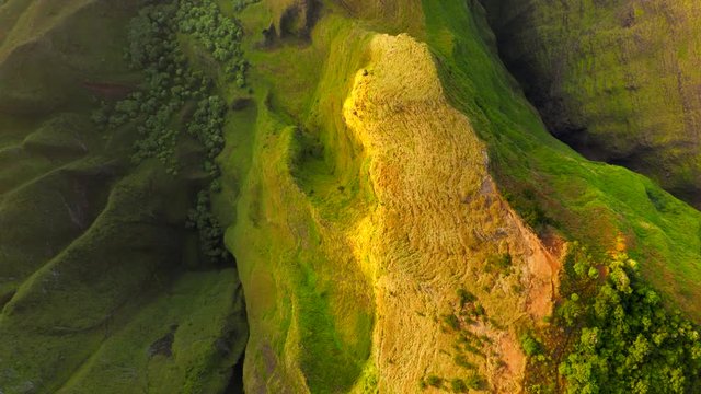 Top view over beautiful exotic grassy rocky ridge, brightly lit by golden rays of setting sun.Fantastic terrain of tropical island in Pacific Ocean with sharp peaks and deep narrow ravines.Aerial, 4K.