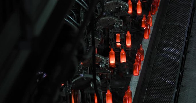 Molten glass mass enters mold and then into glass blower where bottle is formed. Automated conveyor line with process of forming bottle of molten glass. Productionon manufacturing industrial factory.