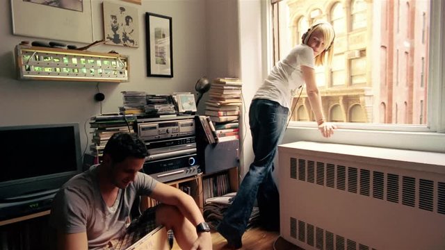 Young man browsing records, attractive woman with headphones sitting on window sill, New York City
