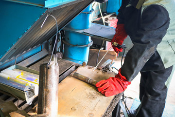 A male worker, a welder in professional work clothes, works on a welding table for the repair and manufacture of parts and spare parts