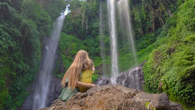 Young woman and her little son tourists visit the biggest waterfall on the Bali island - the Sekumpul waterfall. Travel to Bali concept.