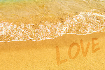 Word love, written in wet yellow sand, covered by a transparent sea wave. Honeymoon, romantic tropical background