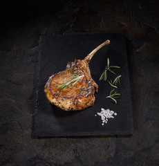 grilled pork steak tomahawk on black slate on a dark background