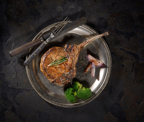 grilled pork steak tomahawk on a platter  on a dark background
