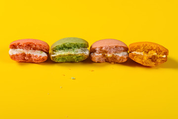 half eaten colorful macaroons on yellow background