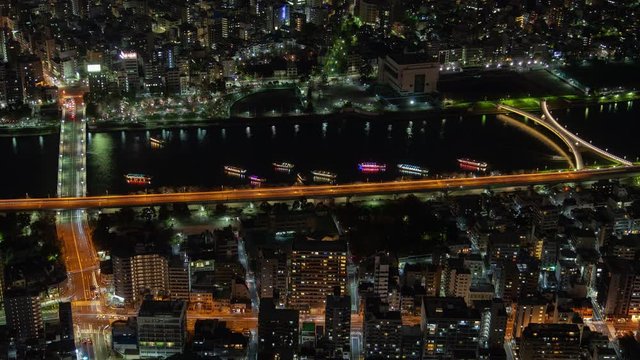 Timelapse Tokyo motorboats arrive and depart with coloured illumination reflected in river near city overpass highway at deep night zoom out