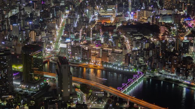 Timelapse illuminated overpass highways with heavy traffic and motorboats sailing on river with bridges and reflecting Tokyo city at night zoom out